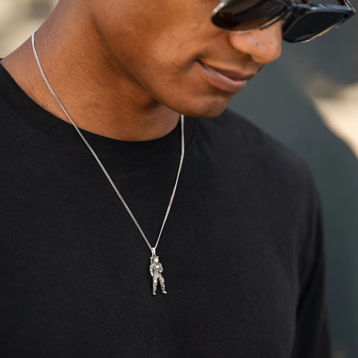 Man wearing a black shirt and sunglasses with a necklace featuring a pendant.