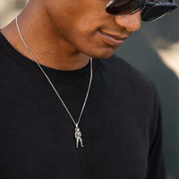 Man wearing a black shirt and sunglasses with a necklace featuring a pendant.