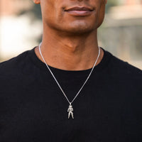 Man wearing a black shirt with a silver necklace featuring a pendant.