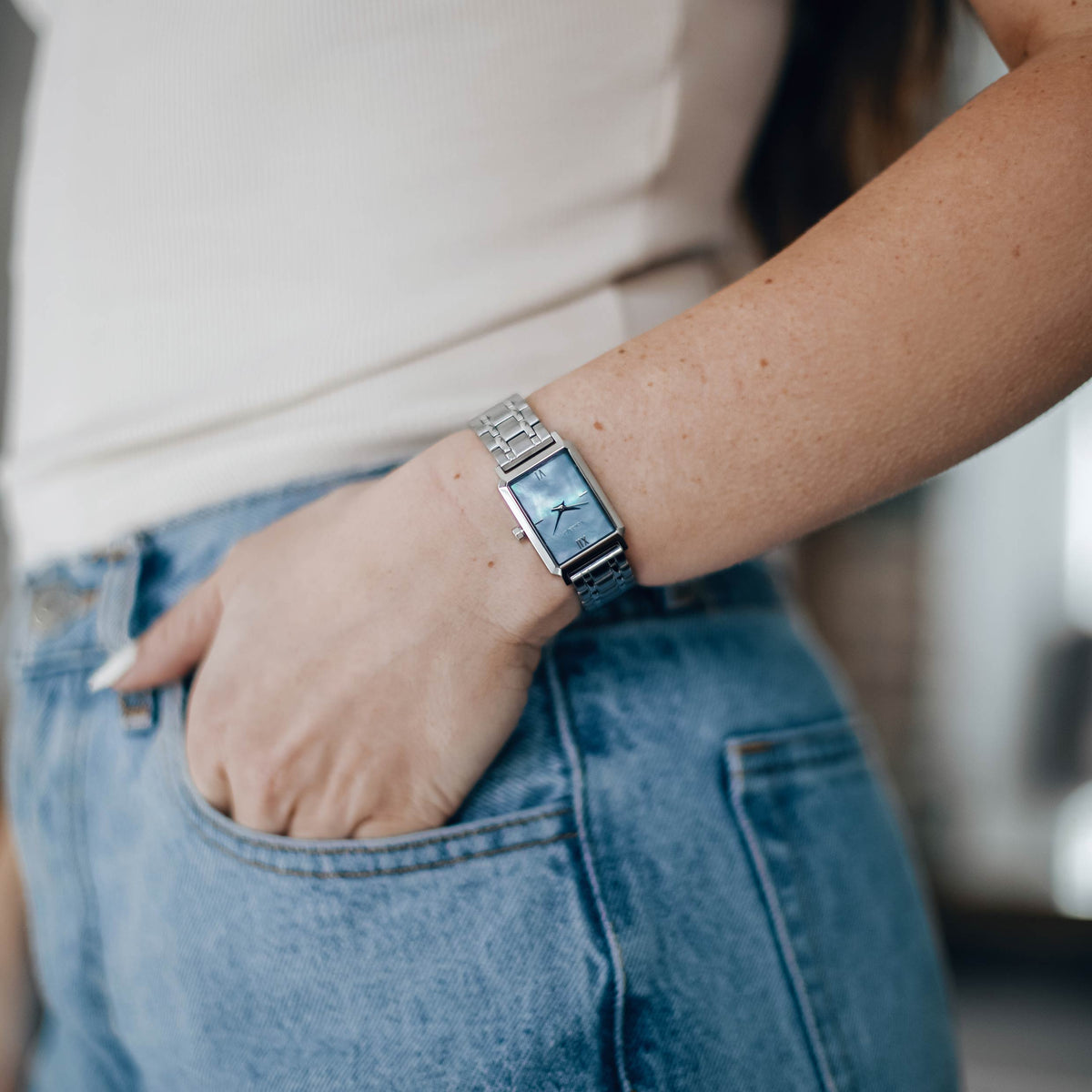 Person wearing a silver watch on a blurred background