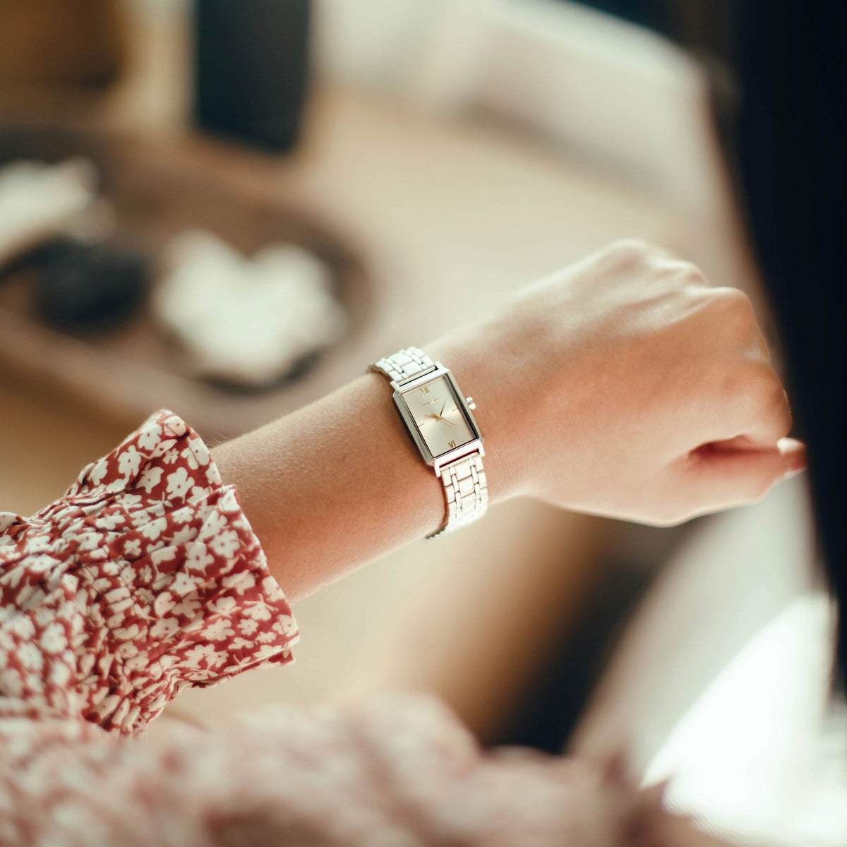 Person wearing a silver watch on a blurred background