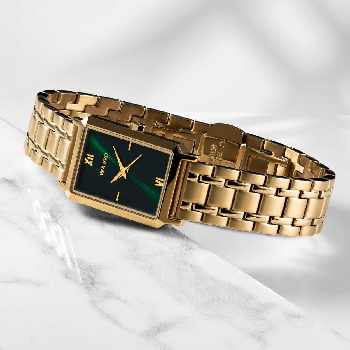 Gold wristwatch with a green face on a marble surface