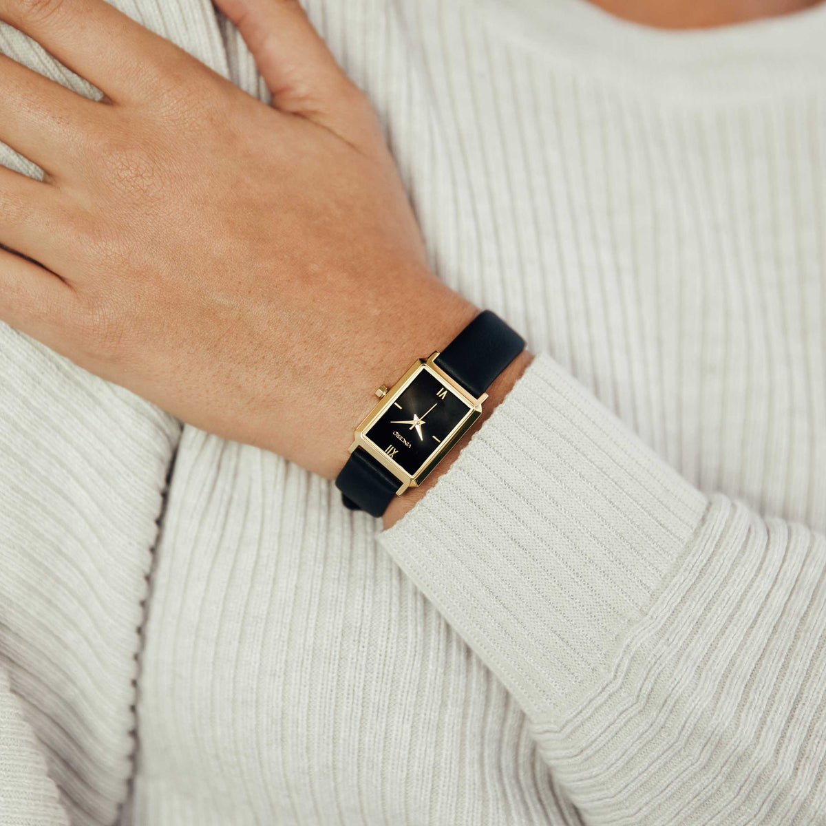 Gold watch with black strap on a wrist against a neutral background