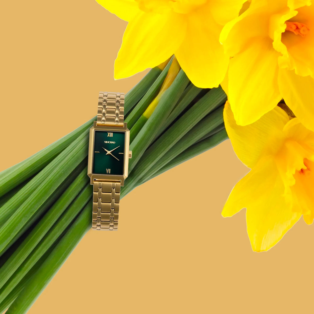 Gold watch on a stem of yellow daffodils with a beige background