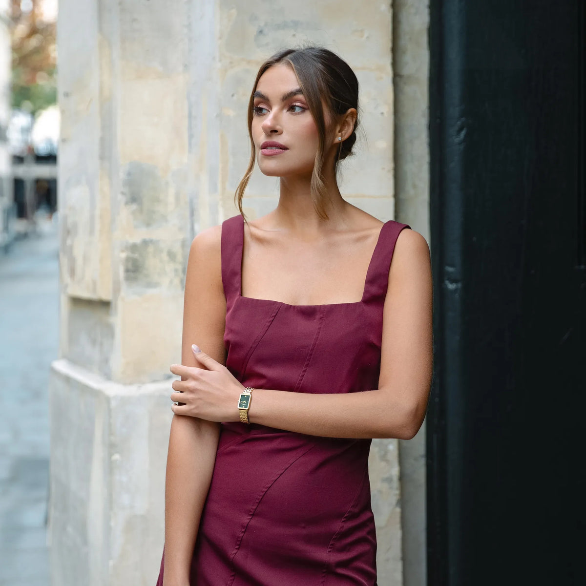 Woman in a burgundy dress standing against a stone wall.