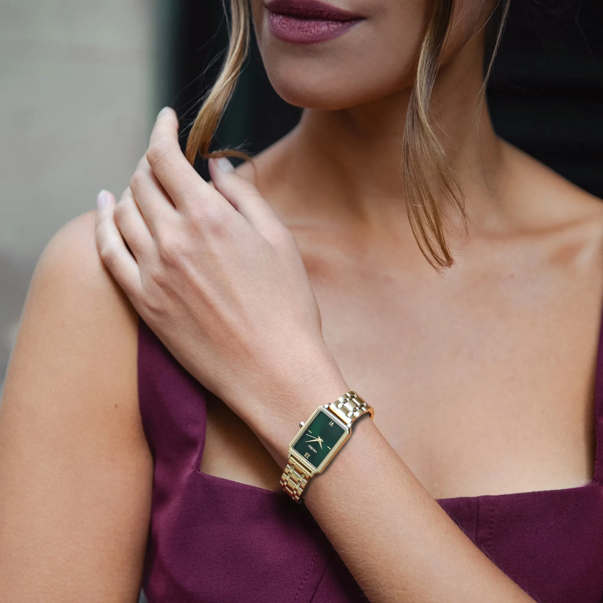Woman wearing a gold watch with a green face on a blurred background
