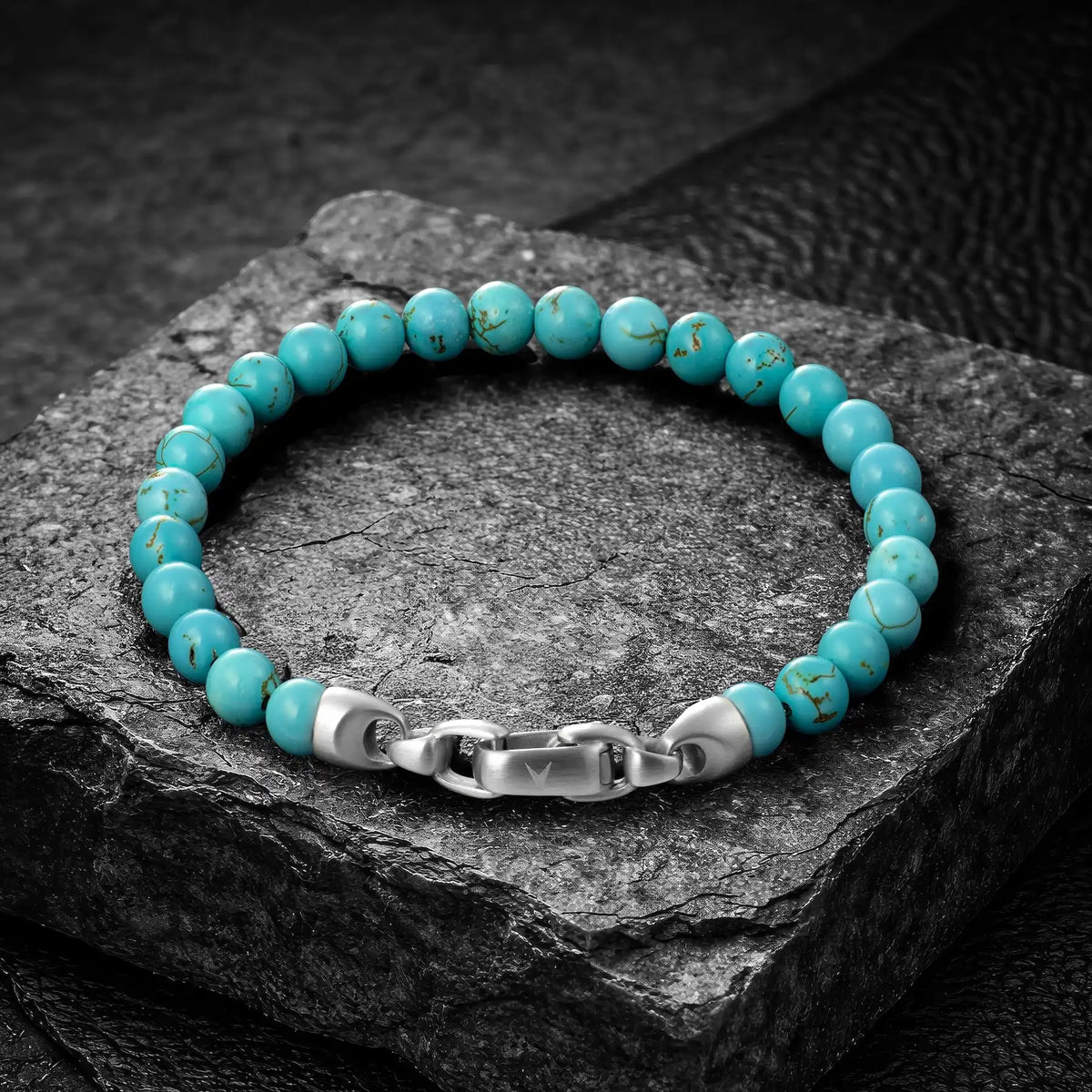 Turquoise beaded bracelet with a silver clasp on a dark stone surface