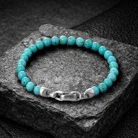 Turquoise beaded bracelet with a silver clasp on a dark stone surface