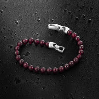Garnet beaded bracelet with silver clasp on a dark textured surface