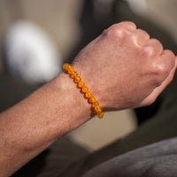 Hand wearing an orange beaded bracelet with a blurred background