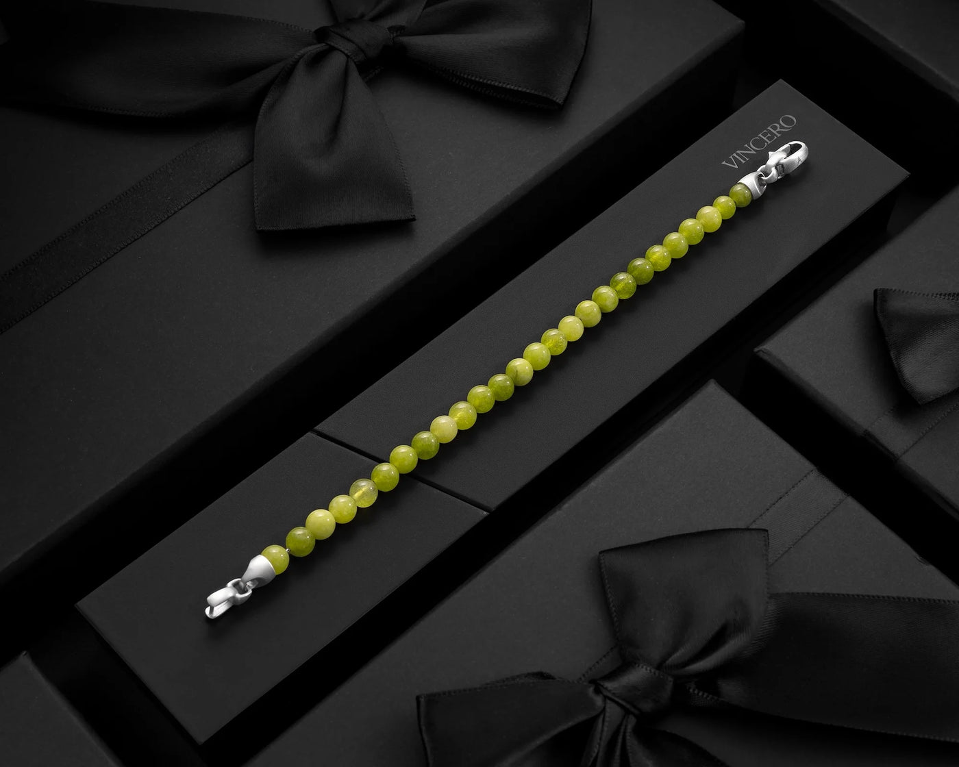 Green beaded bracelet with silver clasp on a black surface with 'Vincenzo' branding.