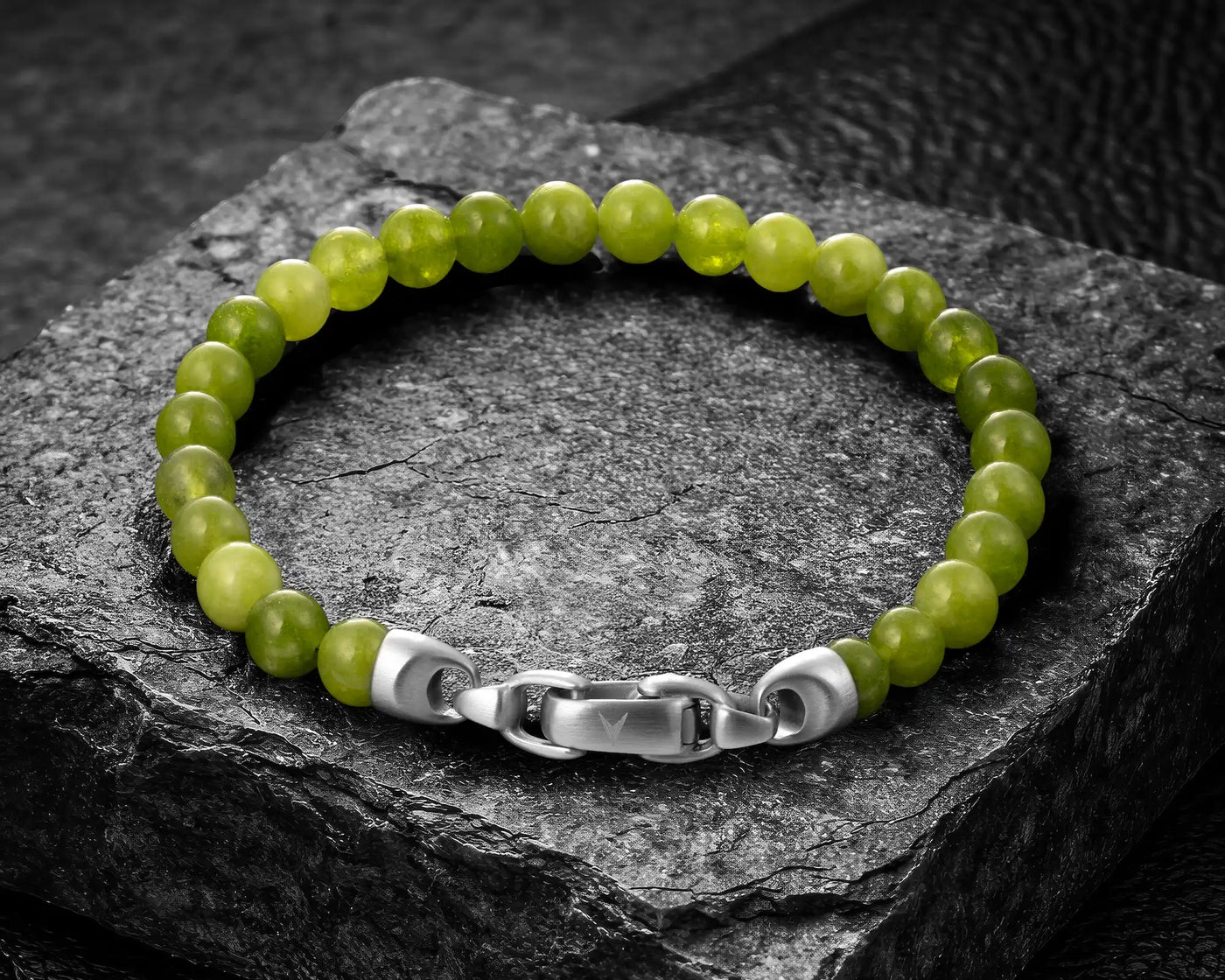 Green beaded bracelet with silver clasp on a dark stone surface