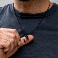 Person holding a small black electronic device with a blue light on a plain background