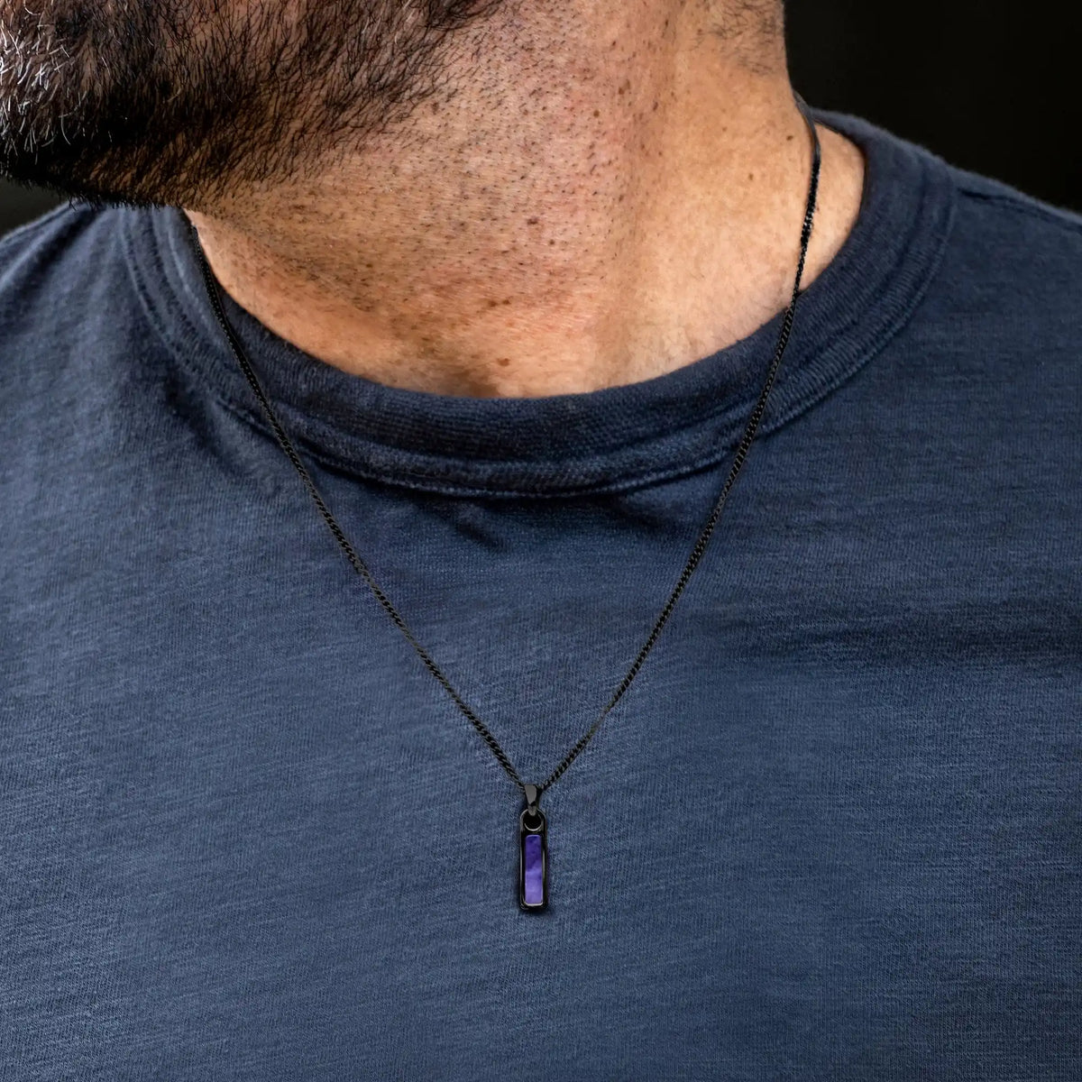 Person wearing a dark blue shirt with a necklace featuring a purple pendant.