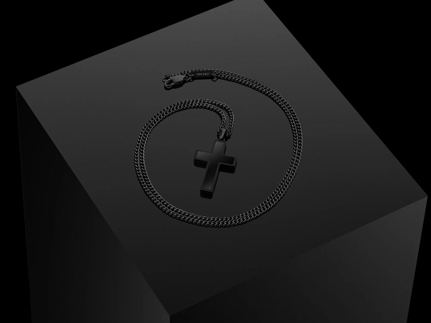 Black cross pendant with a black chain, displayed on a black podium. 
