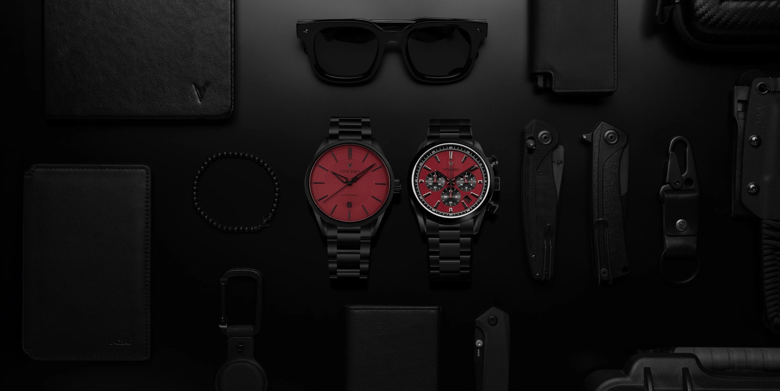 Collection of black and red items including watches, glasses, and knives on a dark surface