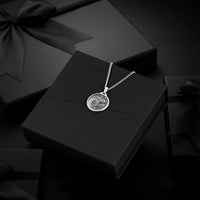 Silver necklace with a pendant on a black box, surrounded by black gift boxes.