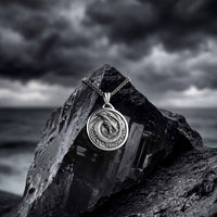 Silver pendant with dragon design on a rock against a stormy sky
