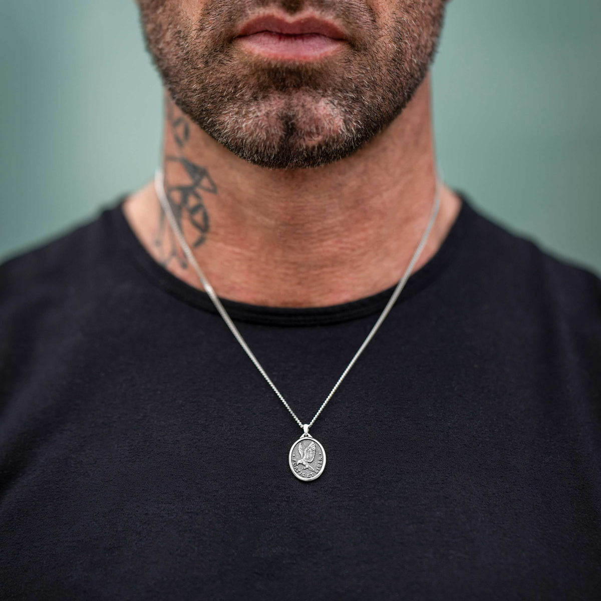 Man wearing a silver chain necklace featuring a detailed silver eagle pendant.