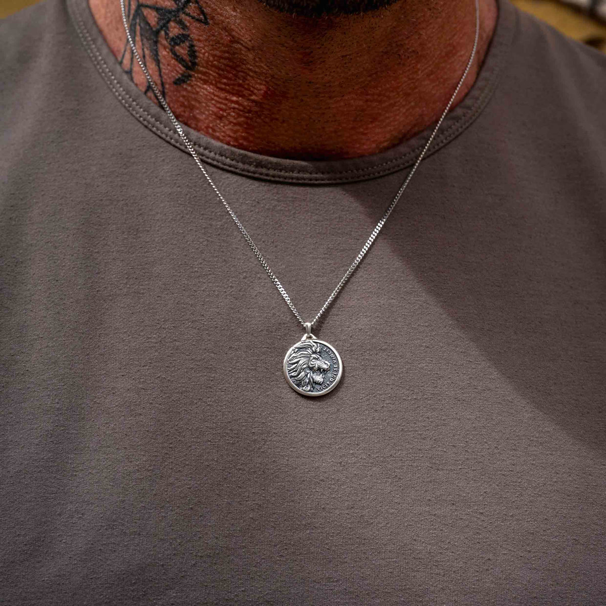 Close-up of a man wearing a silver chain necklace with a silver lion pendant