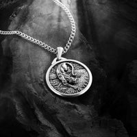 Silver necklace with a round pendant featuring a lion design on a dark stone surface