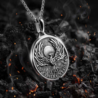 Silver pendant with a phoenix design on a dark background with flames.