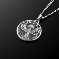 Silver pendant with a phoenix design on a black background