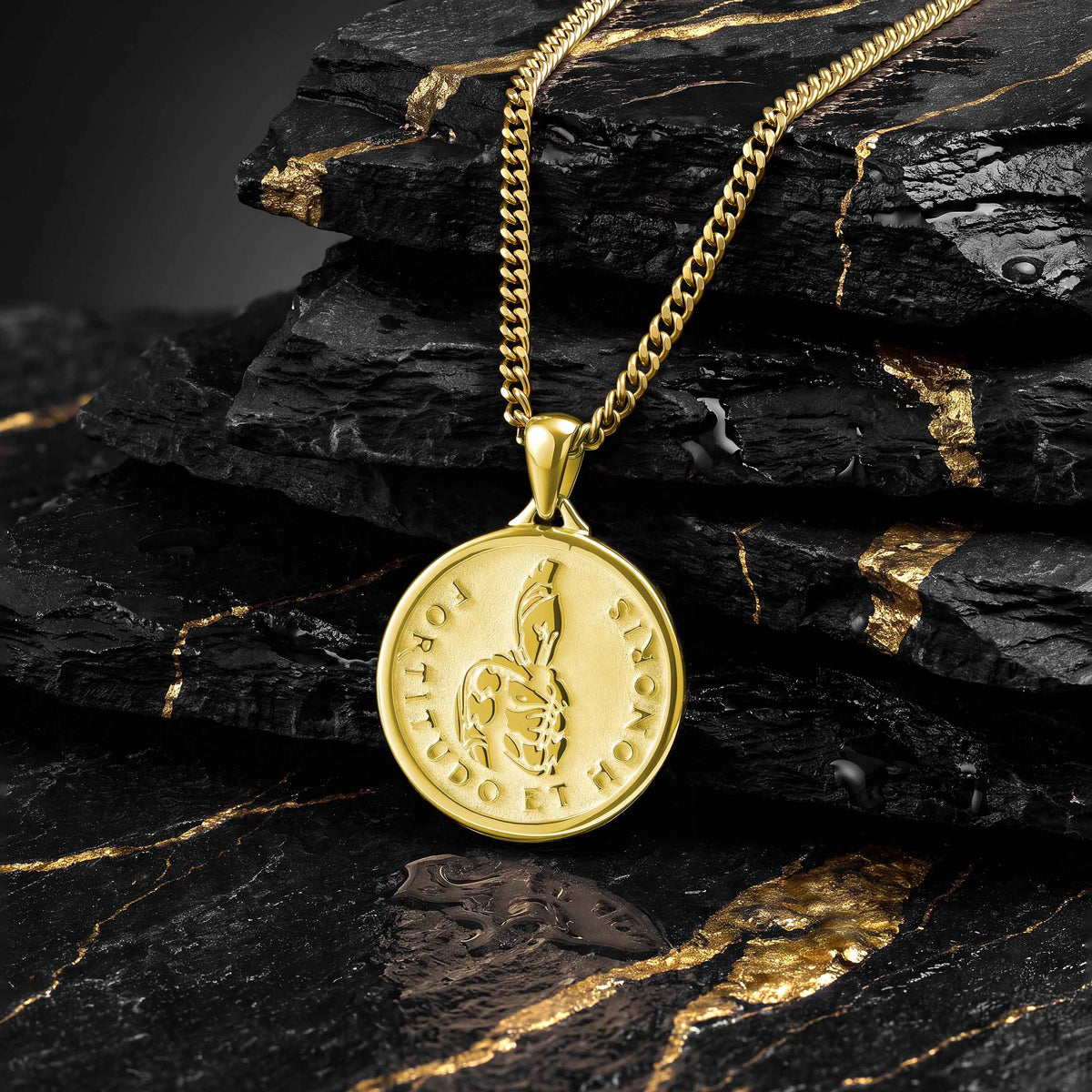 A gold coin pendant necklace featuring a snake wrapped around a cross, with the words 'JESUUS ET MORT' engraved on the side, resting on stacked black and gold marbled rocks.