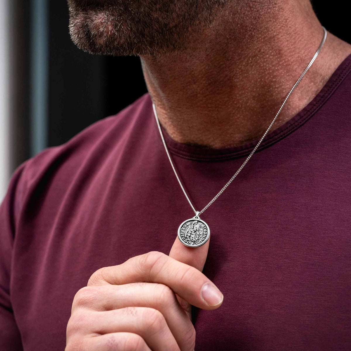 Man wearing silver chain necklace with silver Spartan pendant, using his finger to display the necklace