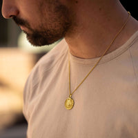 Man wearing a gold necklace with a pendant against a blurred background
