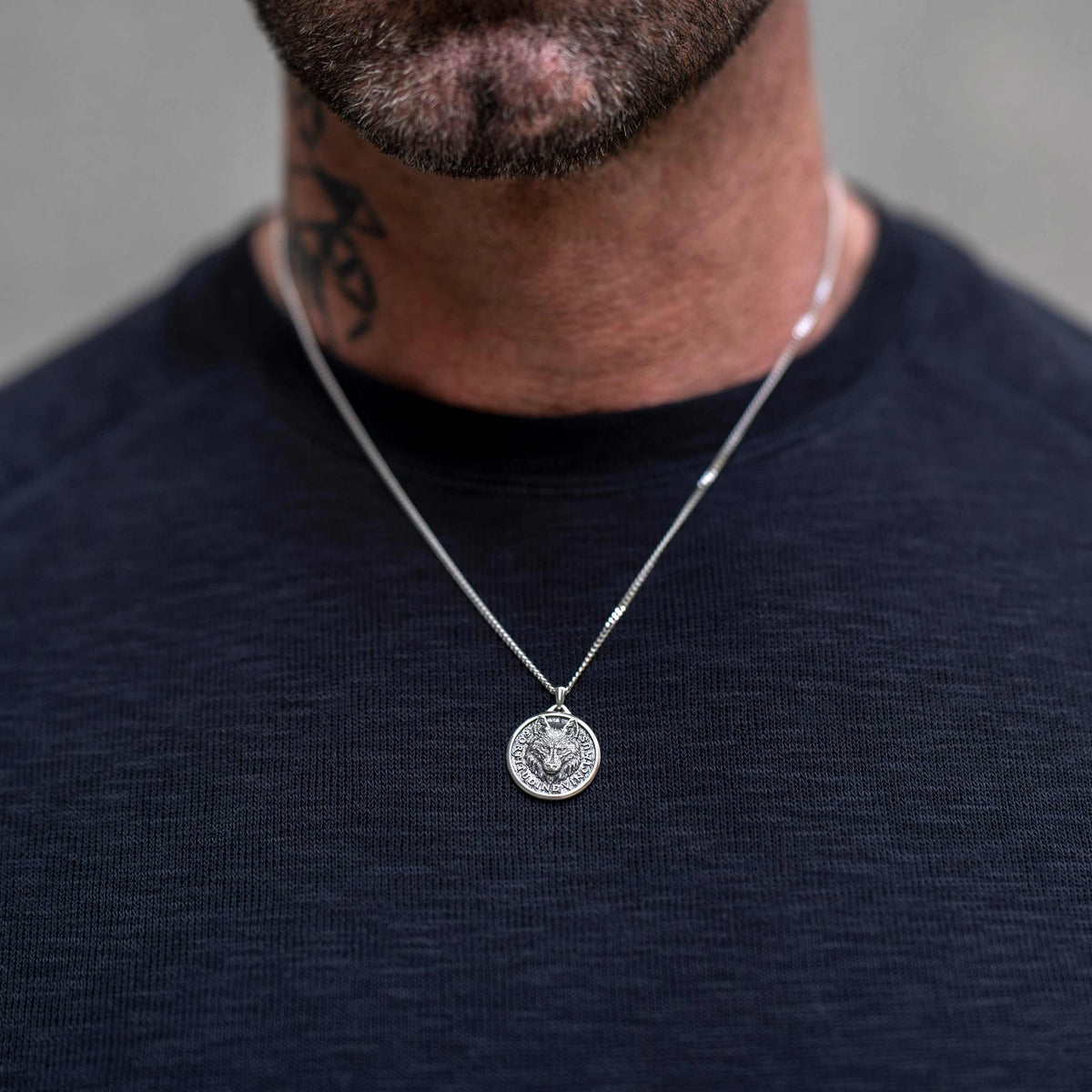 Man wearing silver chain necklace with silver wolf pendant. 