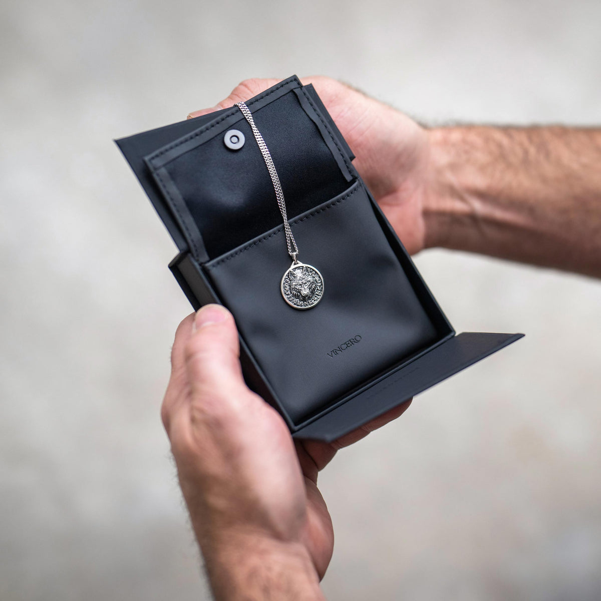 Silver chain necklace with silver wolf pendant, displayed on a black case being held in a man's hands