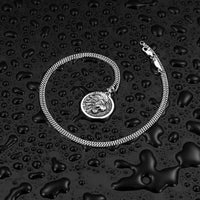 Silver chain necklace with a lion pendant on a black textured surface.