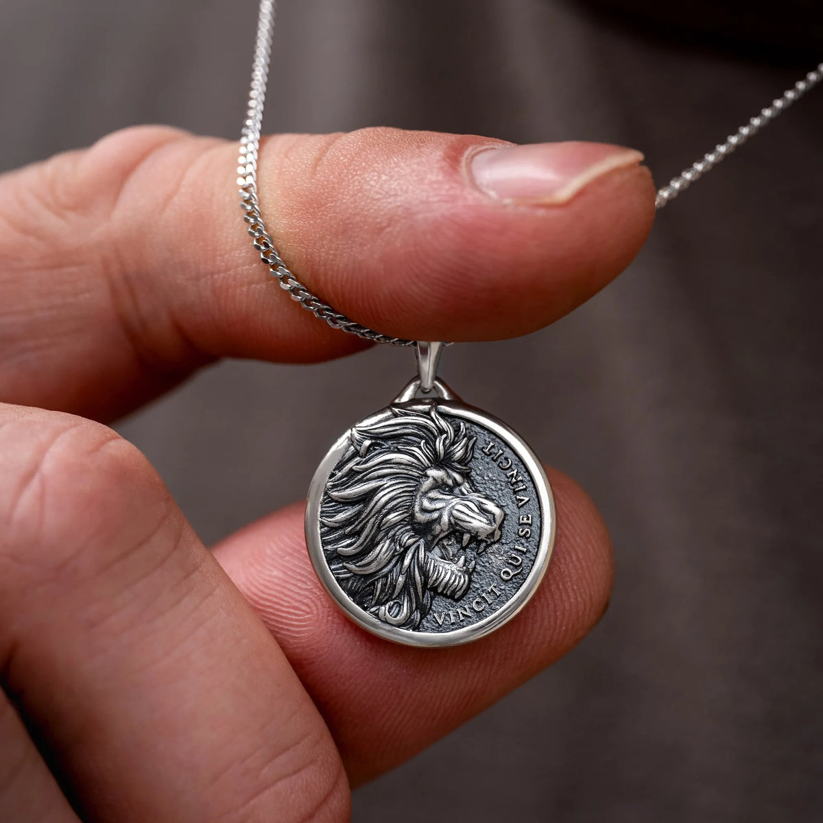 Silver lion pendant necklace held between fingers against a blurred background