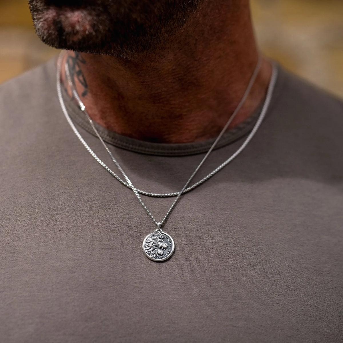 Man wearing a silver necklace with a lion pendant on a blurred background