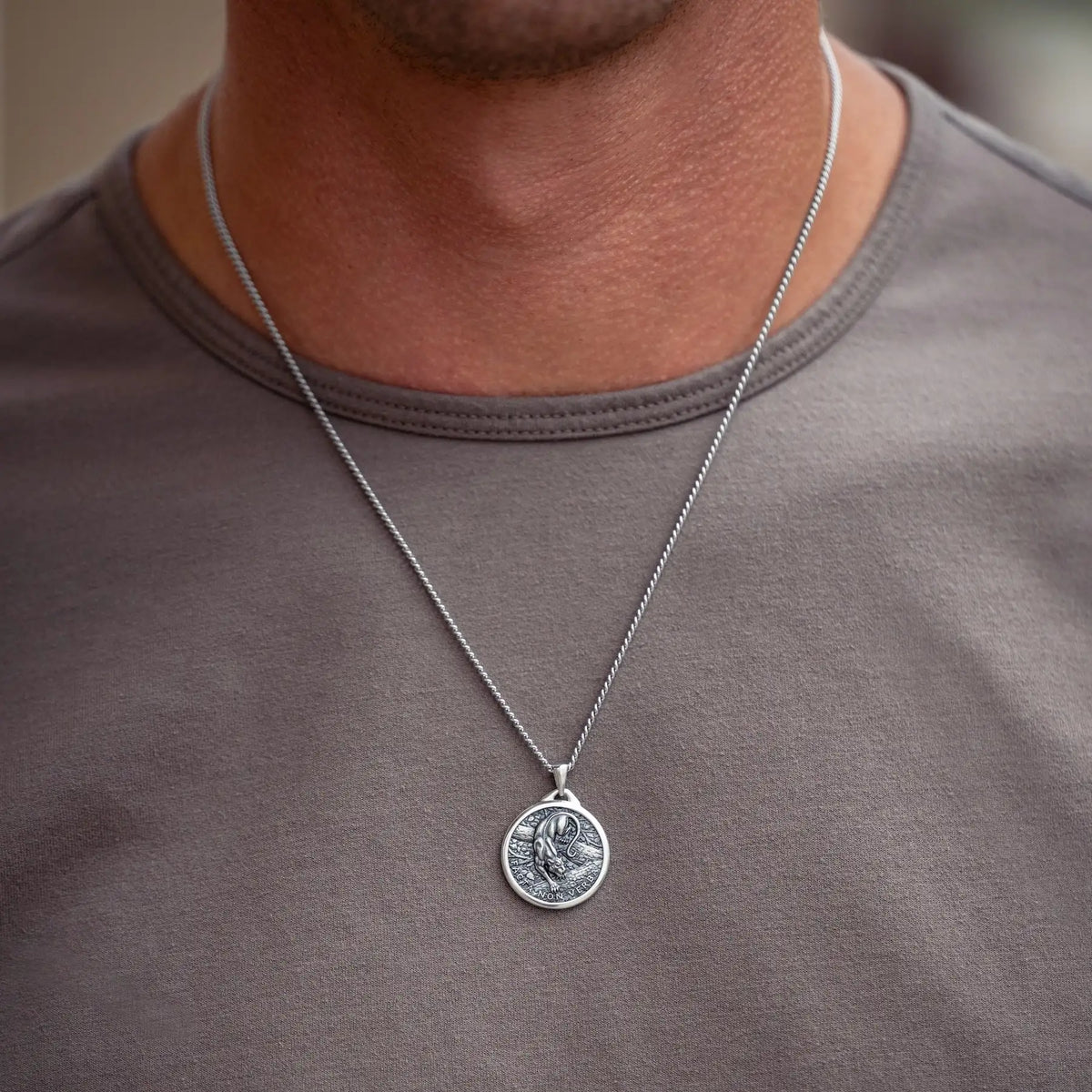 A silver coin pendant necklace worn by a man in a gray t-shirt. The pendant features an embossed design of a panther figure.