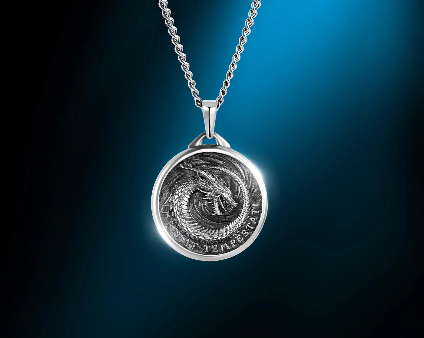 A silver pendant necklace featuring a circular medallion with an engraved dragon design and the text 'QUO TEMPERATUR', suspended from a silver chain against a dark blue gradient background.