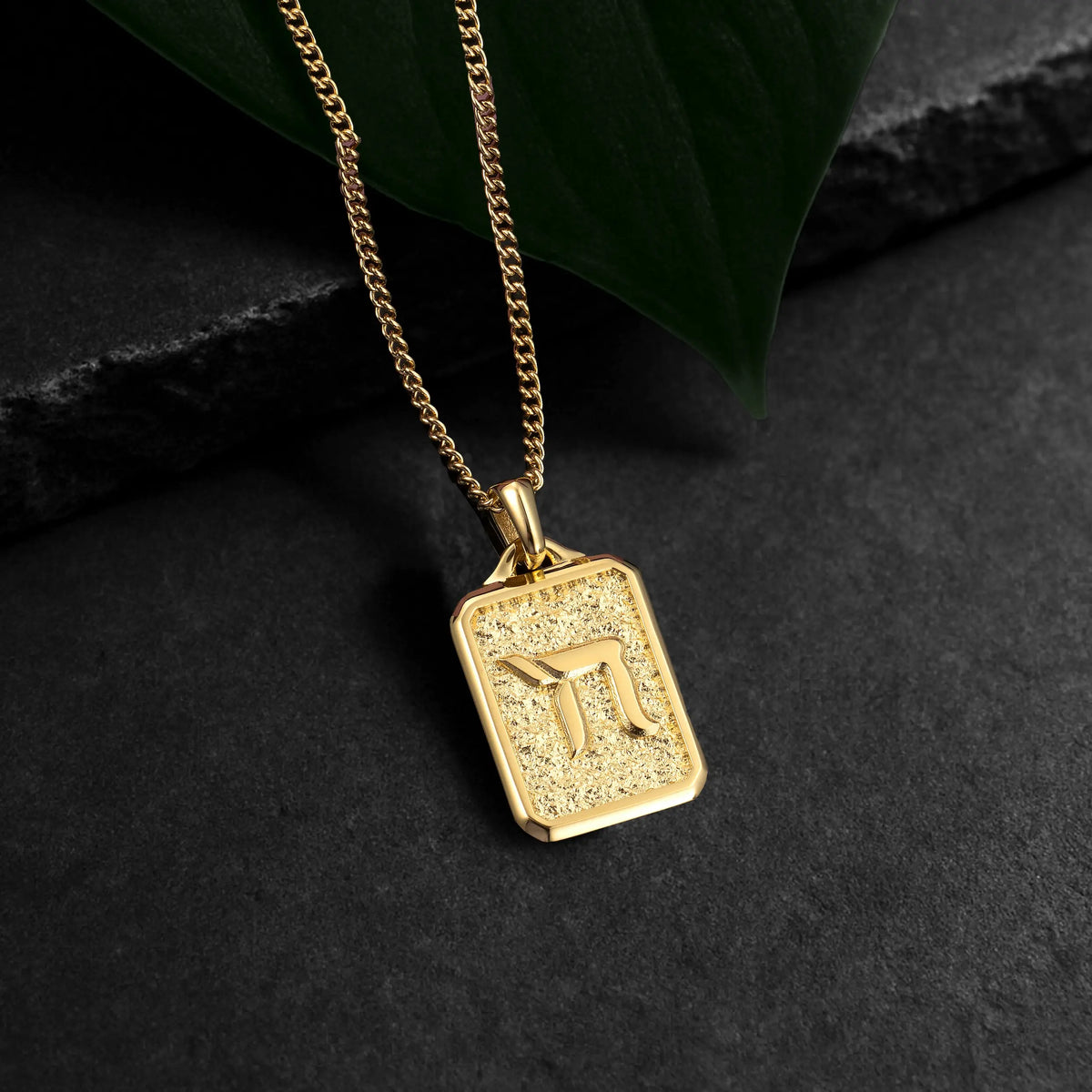 Gold necklace with a square pendant on a dark surface