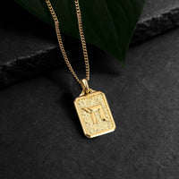 Gold necklace with a square pendant on a dark surface