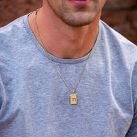 Man wearing a gold necklace with a rectangular pendant against a blurred background