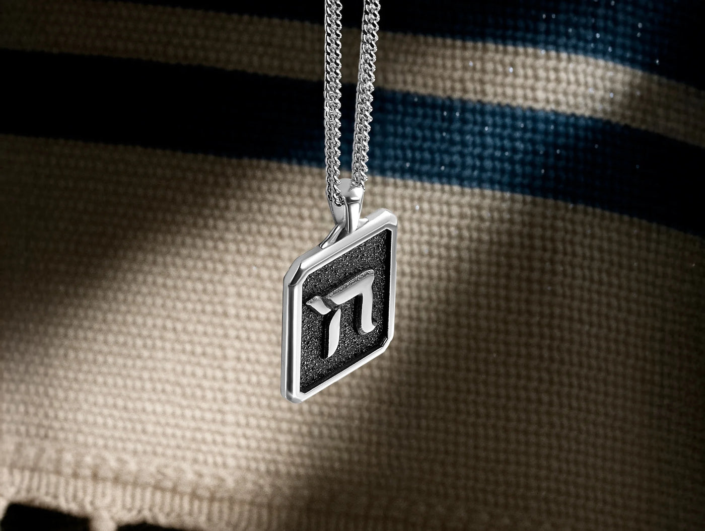 Silver pendant with a geometric design on a textured fabric background