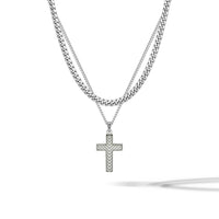 A silver-toned double-layer necklace featuring a thick curb chain and a delicate chain with a textured cross pendant, displayed on a clean white background with a soft shadow.