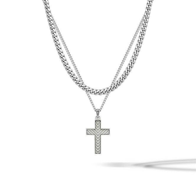 A silver-toned double-layer necklace featuring a thick curb chain and a delicate chain with a textured cross pendant, displayed on a clean white background with a soft shadow.