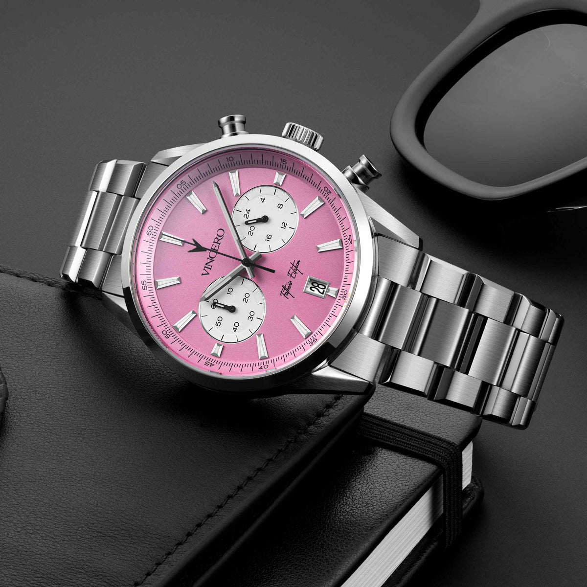 Father’s Edition watch, featuring a pink face, stainless steel casing, and steel band, displayed near sunglasses.