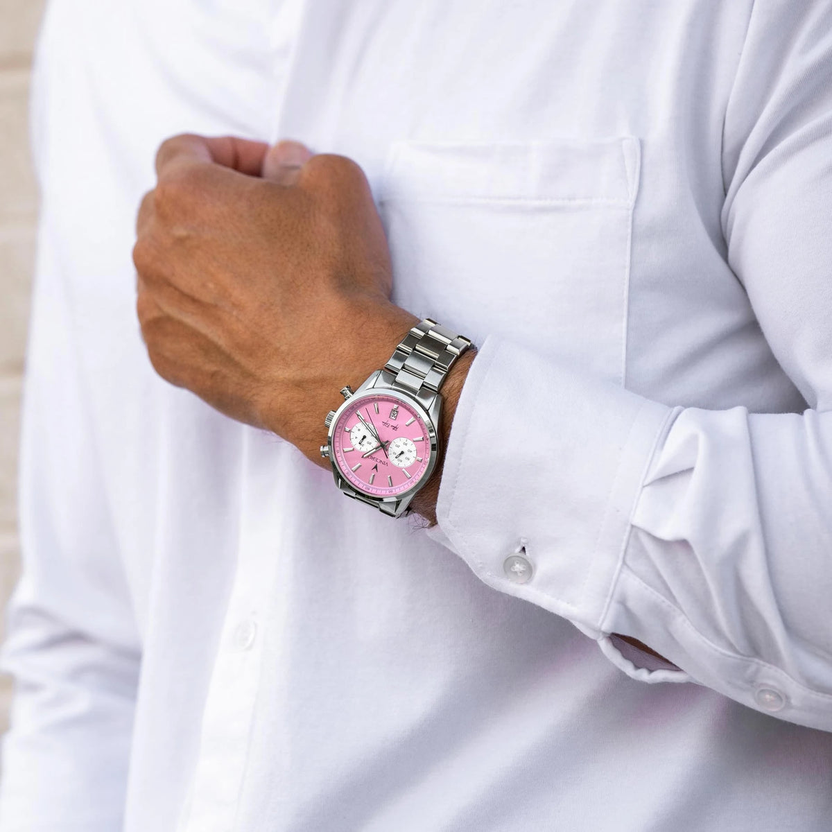 Man with holding his arm in front of his chest, wearing a Father’s Edition watch, featuring a pink face, stainless steel casing, and steel band.
