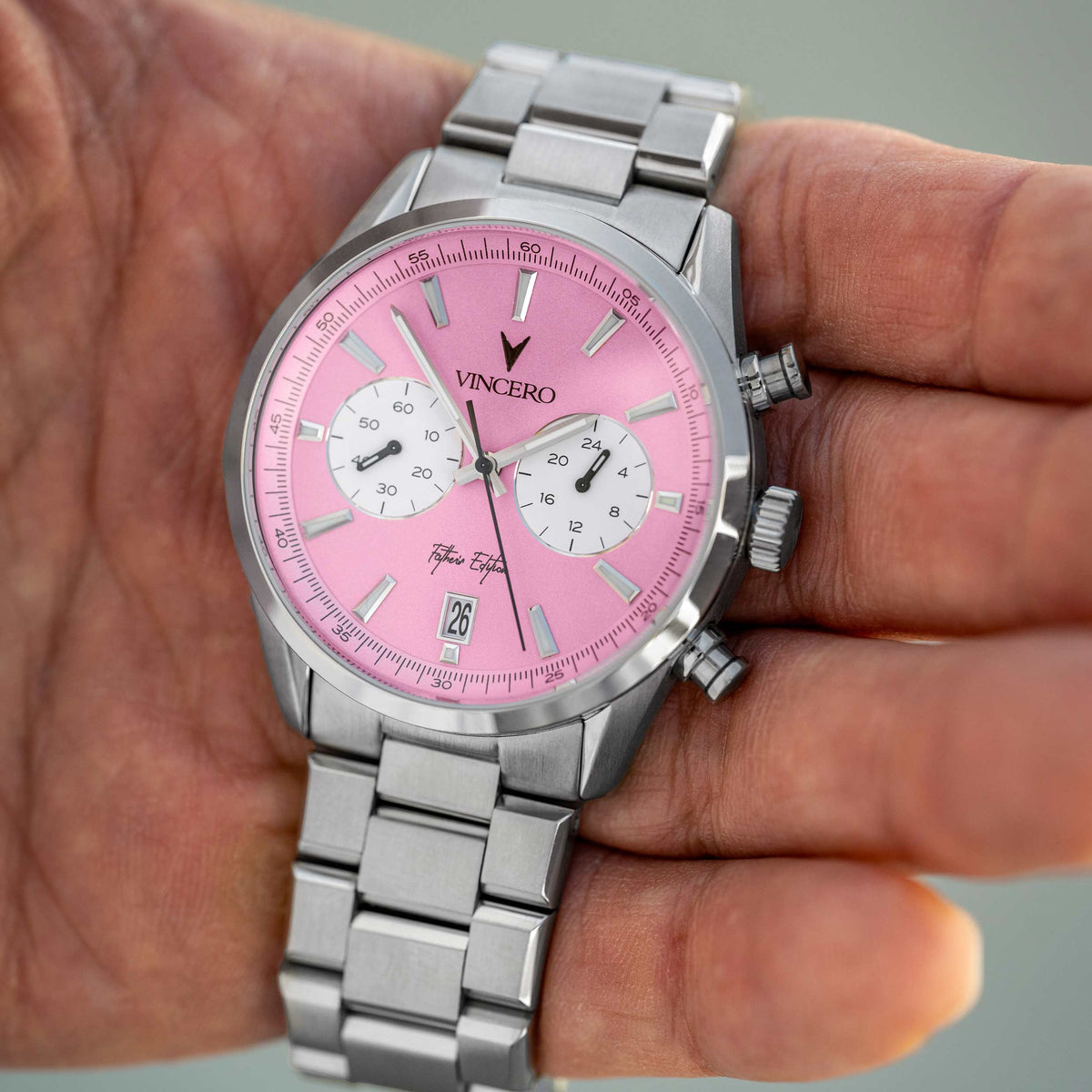 Father’s Edition watch, featuring a pink face, stainless steel casing, and steel band, displayed in a man's hand. 