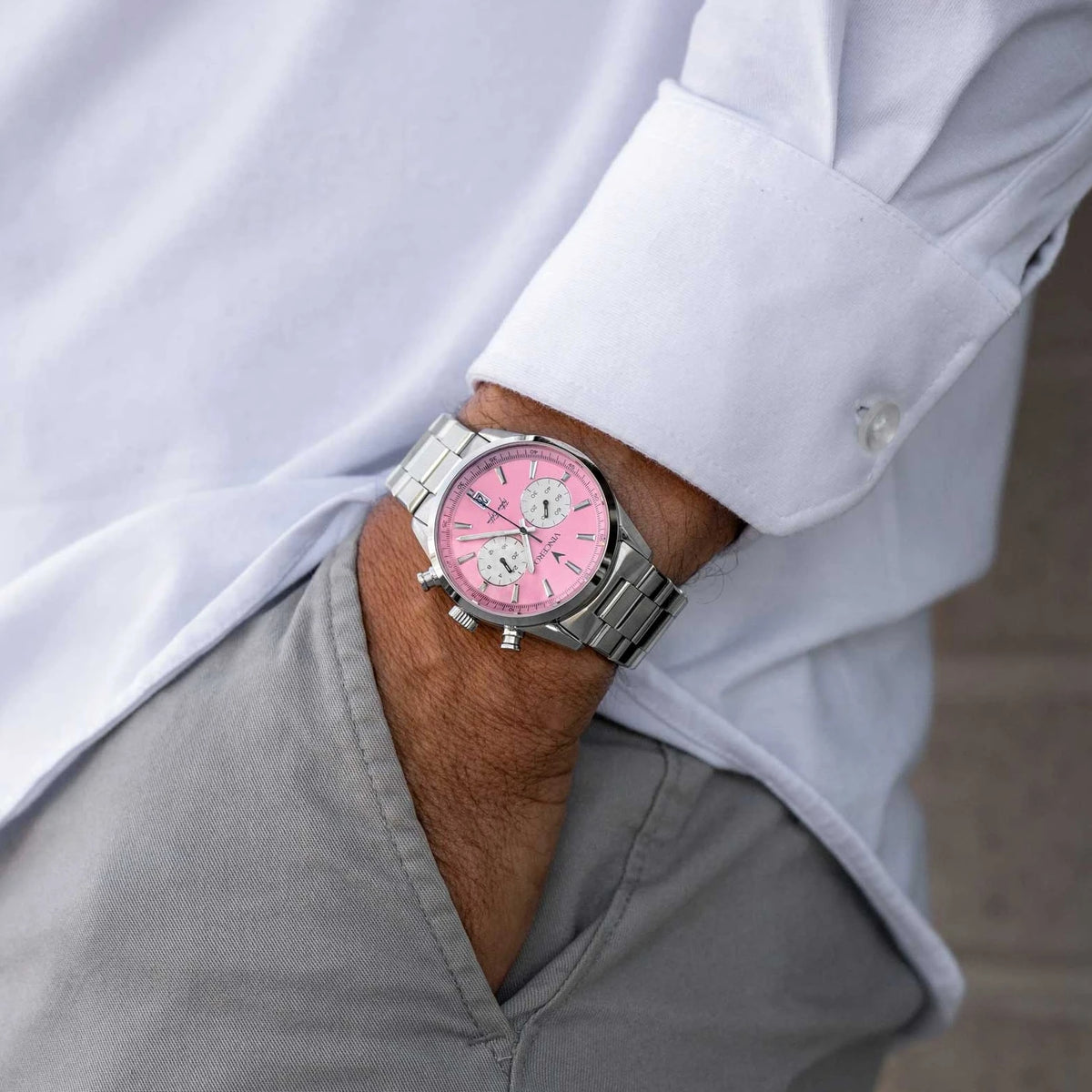 Man with hand in his pocket wearing a Father’s Edition watch, featuring a pink face, stainless steel casing, and steel band.
