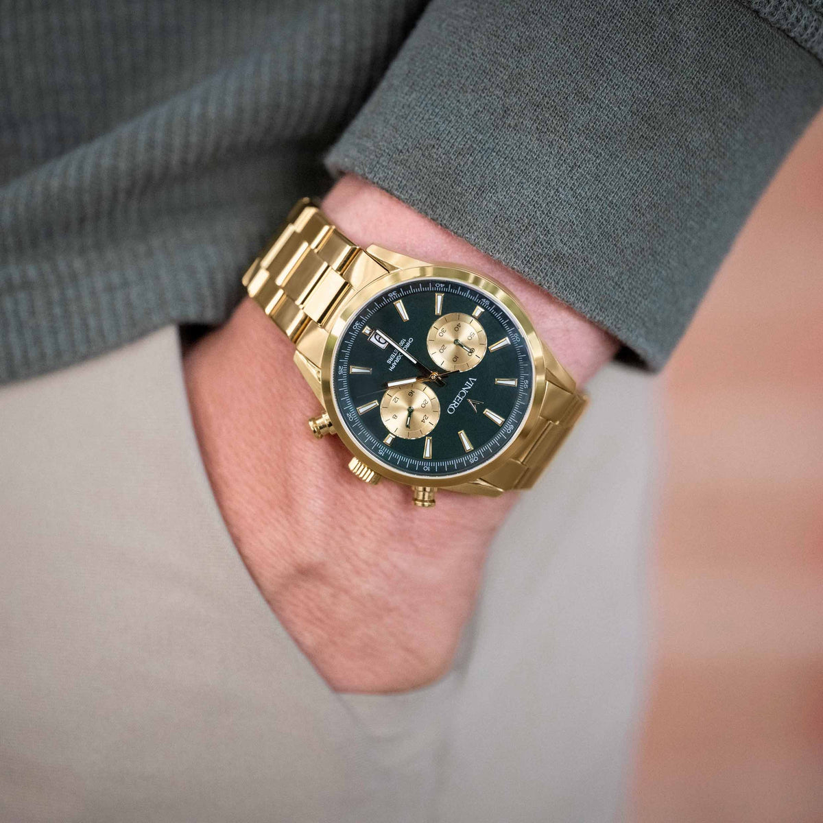 Gold wristwatch with a dark face on a person's wrist, wearing a gray suit.