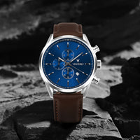 Watch with a blue face and brown leather strap on a rocky surface