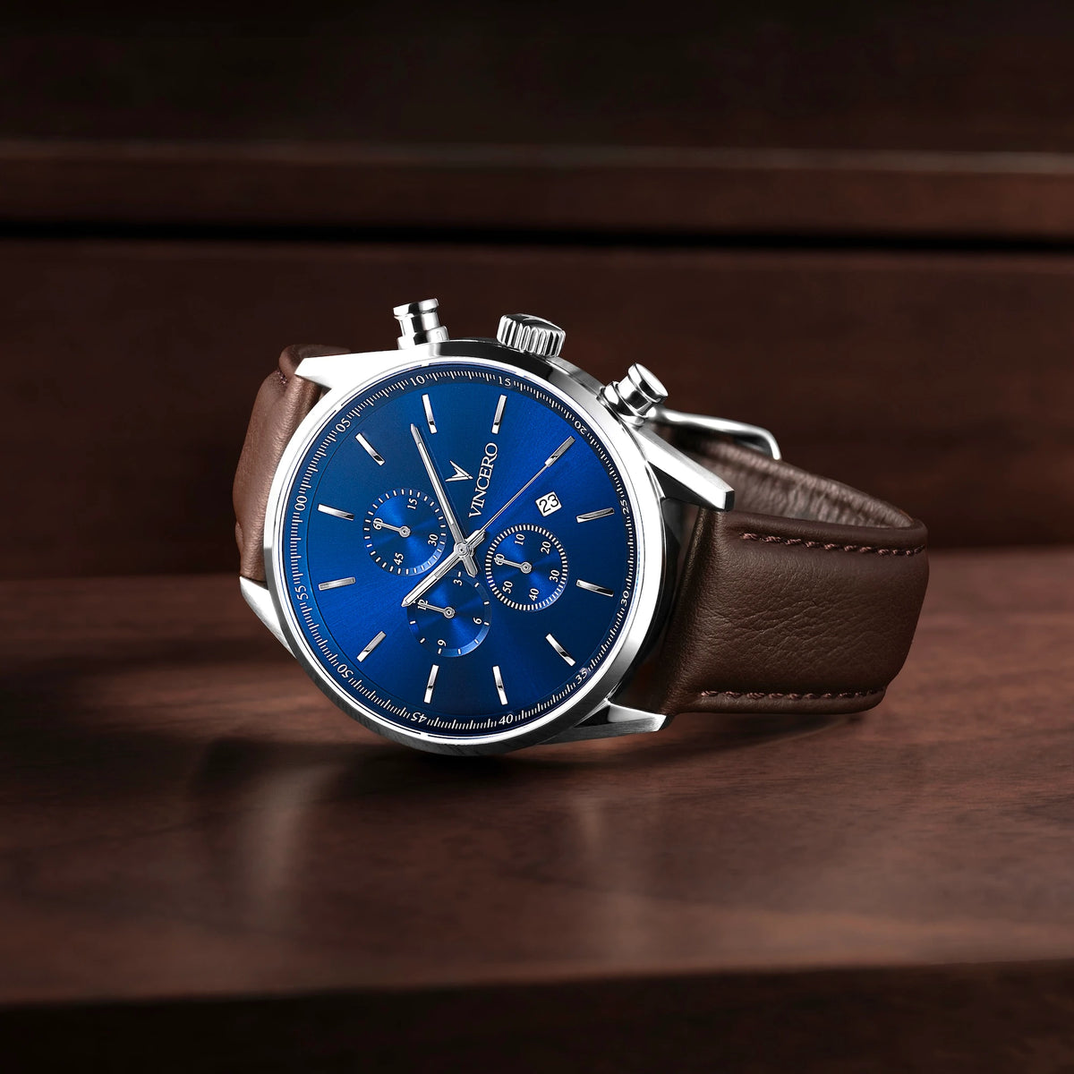 Watch with a blue face and brown leather strap on a wooden surface